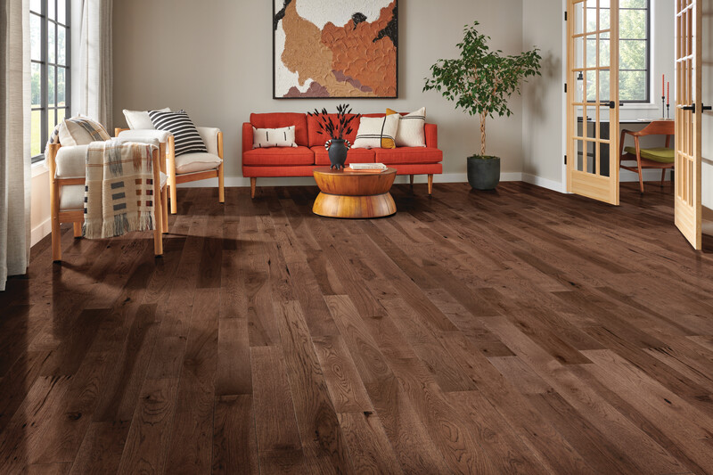 Sitting area with multi-toned hardwood flooring, a red couch, chair, and potted tree